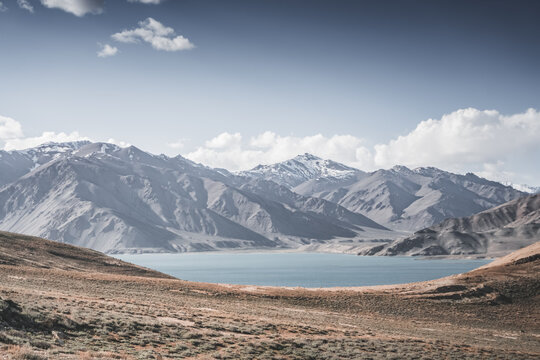 Landscape in the Pamir Mountains with a blue lake Yashilkul in the Tien Shan, a panoramic view of the highlands with snow-capped rocky peaks and the blue waters of the lake