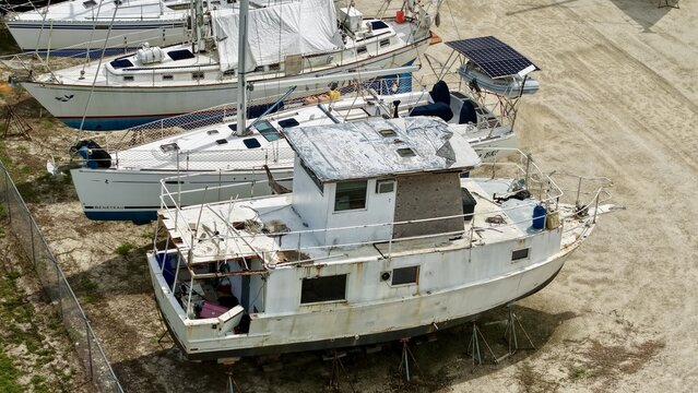 Aerial view of sailboats and a motorboat resting on stands in a dry storage boatyard under bright daylight in Green Cove Springs, Florida, United States.