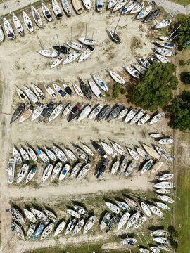 Aerial view of numerous sailboats parked in rows at a dry storage boatyard surrounded by green trees in Green Cove Springs, Florida, United States.
