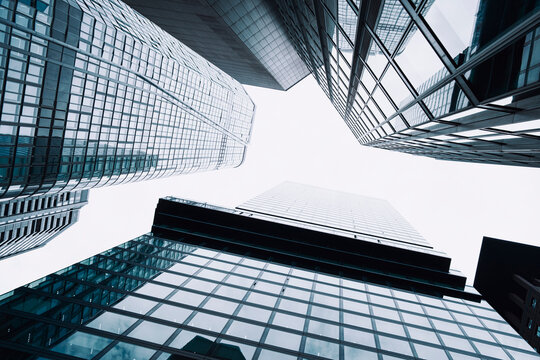 Upward view of glass skyscraper architecture creates a canyon between urban towers, where facades converge around bright sky and sharp lines.