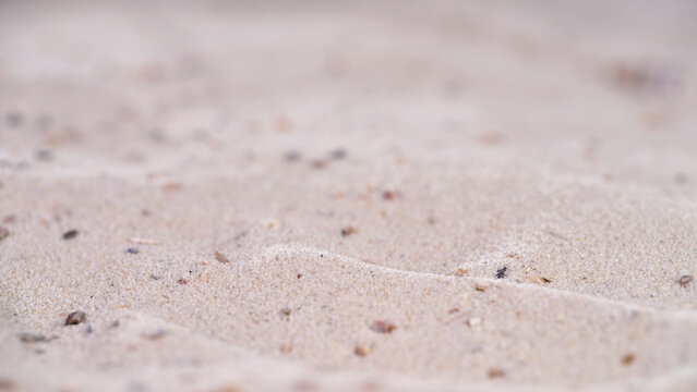 Sand patterns on beach with small stones and shells at low tide during daylight near ocean waves