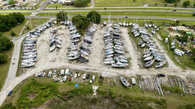Aerial view of a boatyard with numerous sailboats parked in rows surrounded by lush green trees and a nearby road in Green Cove Springs, Florida, United States.
