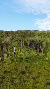 Cinematic rotating view of cascading waterfalls and lush volcanic cliffs at Poco da Ribeira do Ferreiro in the Azores Portugal