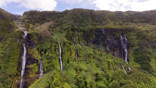 Cinematic panoramic view of cascading waterfalls descending through vibrant volcanic landscape at Poco da Ribeira do Ferreiro in the Azores Portugal