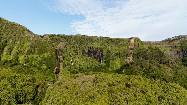Cinematic wide aerial landscape of cascading waterfalls flowing through lush volcanic cliffs at Poco da Ribeira do Ferreiro in the Azores Portugal