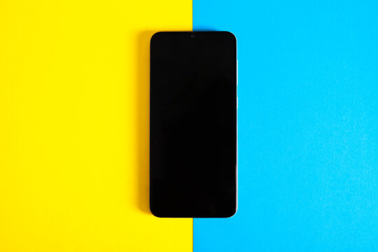 Smartphone with black screen on yellow and blue background. Top view