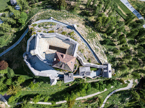 Aerial view of Schloss Tarasp on a rocky hilltop surrounded by lush green trees and winding paths Scuol, Graubunden, Switzerland.