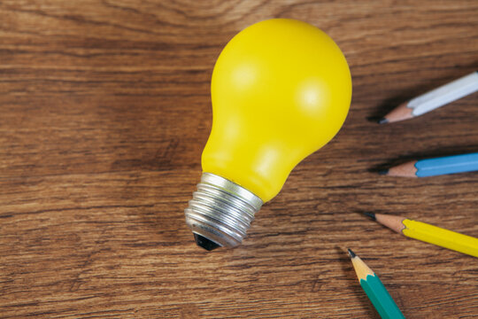 Light bulb and pencils on wooden background, business idea concept.