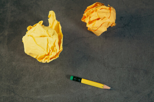 Yellow crumpled paper ball and yellow pencil on black background.