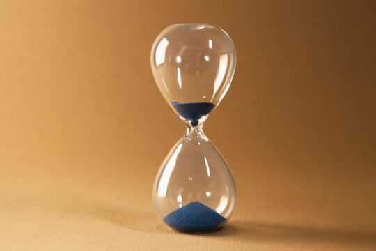 Hourglass with blue sand on brown background, time passing concept.