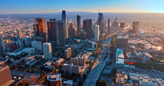 Cinematic aerial view of downtown Los Angeles skyline and busy freeway at sunset with golden light.