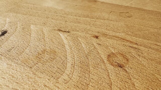 Close-up of a light wooden tabletop surface with visible grain, warm sunlight, subtle scratches, and natural timber texture detail.