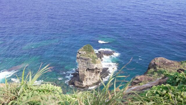 High angle shot of a majestic giant rock standing in the blue ocean near steep cliffs, Yonaguni Island, Japan