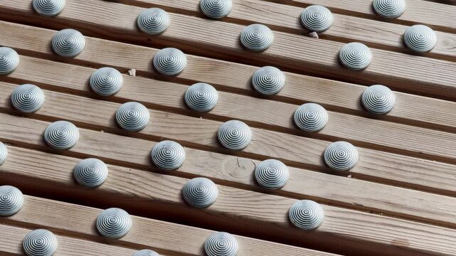 Close-up of tactile metal studs on a wooden slatted walkway, showing an accessibility guidance surface, anti-slip texture, and public pedestrian design detail.