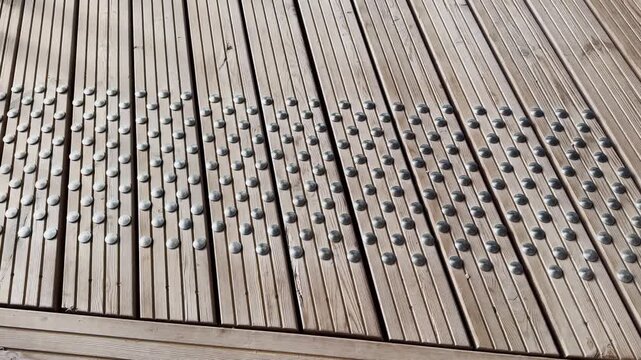 Tactile metal studs on a wooden boardwalk, showing an accessible pedestrian guidance surface with raised warning dots, timber slats, and public pathway design.