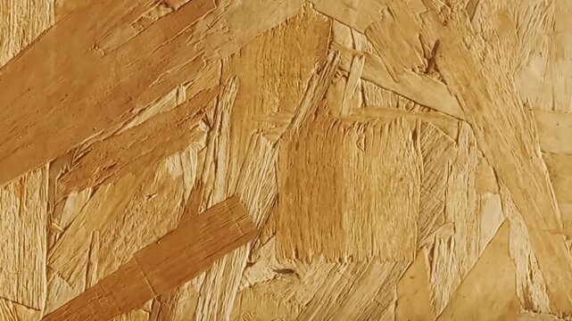 Close-up of oriented strand board surface with compressed wood flakes, rough chip texture, warm yellow tones, and construction material detail.