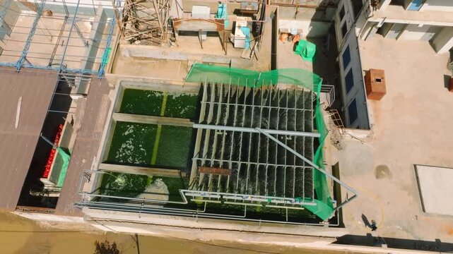 Aerial - rooftop algae cultivation pools and pipe framework greenhouse at industrial facility in Karachi