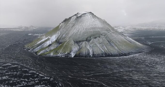 Maelifell volcano rising from black sands in Myrdalsjokull Highlands, Iceland, during snowstorm, showing hyaloclastite geology, glacial erosion and subglacial volcanic terrain, orbit parallax shot.