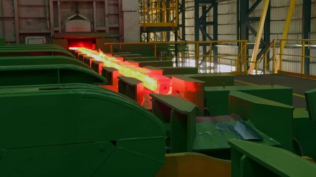 Glowing red hot steel billet rolling along conveyor system during production process in industrial steel mill