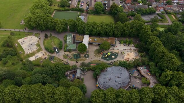 Lloyd park playground, Walthamstow drone orbit reveals skate park, climbing frames, play surfaces, paths and surrounding woodland in an urban London park setting.