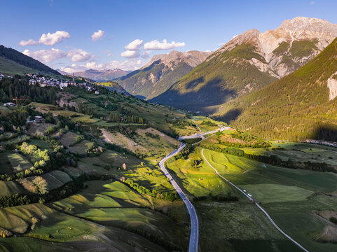 Aerial view of Reformierte Kirche San Lurench and the village of Sent nestled in an Alpine valley with winding roads and rugged mountain peaks Sent, Graubunden, Switzerland.