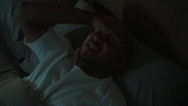 Young man lying awake in bed struggling with insomnia and depression at night. Mental health, Stress sleep disorder. Emotional exhaustion and wellness concept.
