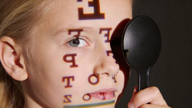 Сlose-up shot of a girl holding an eye occluder paddle to test her vision at an optometrist office. Children ophthalmology and eye exam concept
