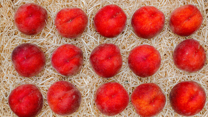Fototapeta premium Fresh peaches arranged on a bed of straw in a market setting during midday