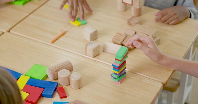 Close view of young pupils using hands to stack colorful tiles and wooden blocks on desk, practicing STEM teamwork, class activity, problem solving, and back to school learning routine daily.
