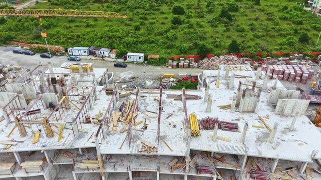 Workers are building a structure where construction materials are scattered. Nearby, homes are visible on a grassy hill. The site shows activity and development.