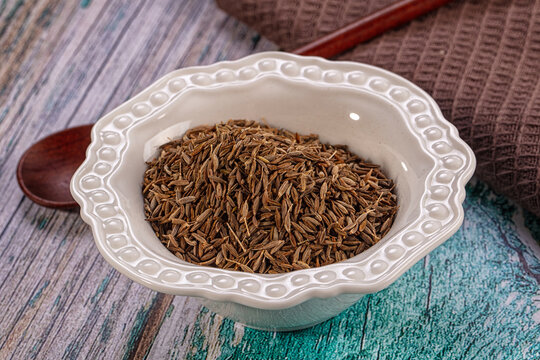 Dry cumin seeds in white ceramic bowl on rustic wooden background