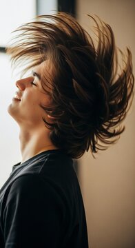 Young man shaking head with long hair flying, joyful expression, natural light