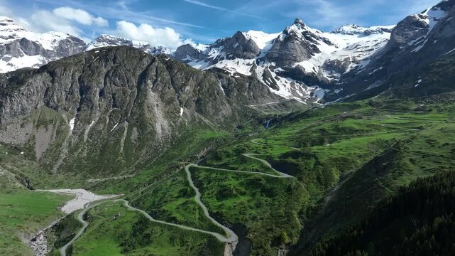 Aerial panorama of winding mountain road and green valley below jagged snowy Pyrenees peaks