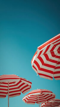 Row of vibrant red and white striped beach umbrellas against a perfectly clear turquoise blue sky background in a minimal summer vacation concept shot focusing on sun protection and holiday vibes