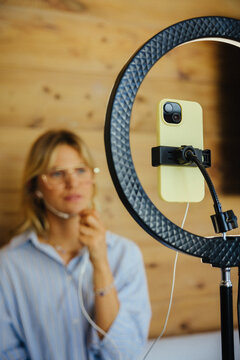 Young woman creating online content with ring light and smartphone
