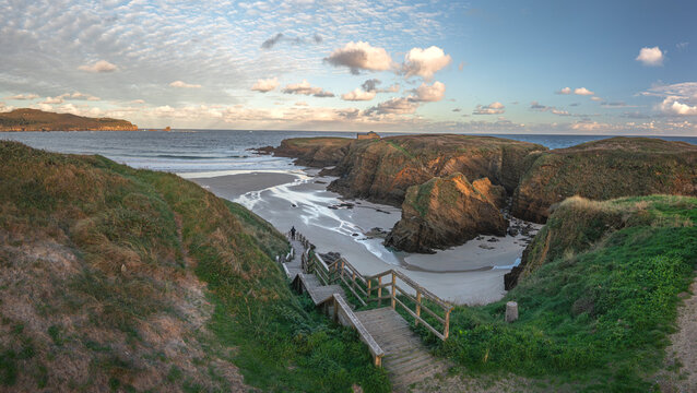 Aerial view of Ermita de Santa Comba on a rocky island with a person on a wooden staircase leading to a sandy beach and rugged cliffs Covas, La Coruna, Spain.