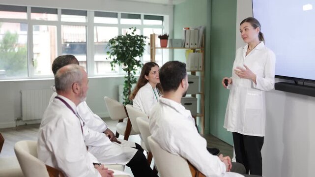 Qualified female doctor holds a remote control in her hands and gives a lecture to doctors in the auditorium. Process of advanced training for doctors. High quality 4k footage