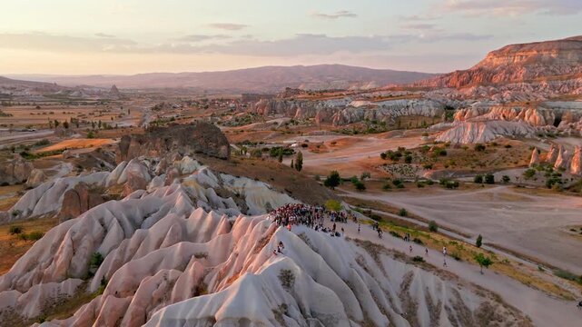 Aerial view of Rose Valley, Cappadocia, Turkey at sunset. Tourists gather with ATVs for quad biking among fairy chimneys and soft pink rock valleys.