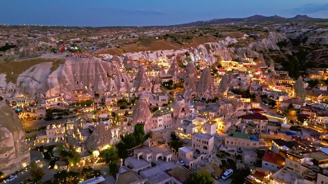 Aerial view of Goreme, Cappadocia, Turkey. Fairy chimneys and cave rocks rise above warm village lights at twilight.