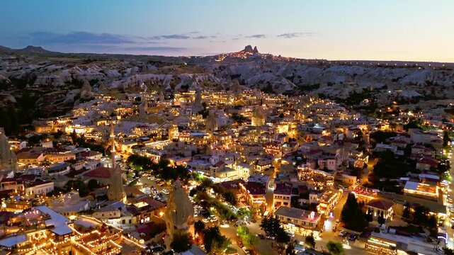 Aerial view of Goreme, Cappadocia, Turkey at night. Warm lights spread across cave houses, stone buildings and rocky valleys.