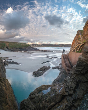 Aerial view of the rugged coastline near Ermita de Santa Comba with a sandy beach, rocky cliffs, and a wooden staircase in Covas, La Coruna, Spain.