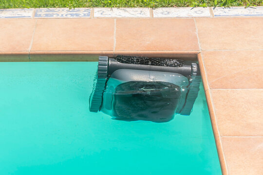 A cordless robot is cleaning the edge of an in-ground pool
