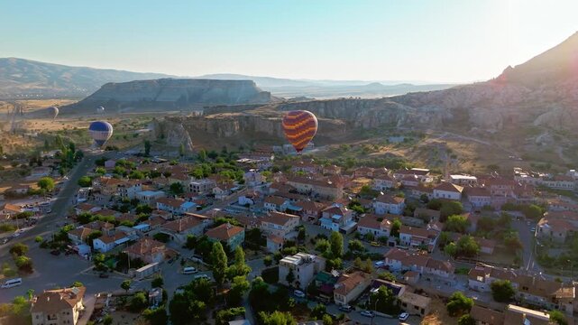 Drone view of Cappadocia, Turkey. A hot air balloon floats over village rooftops, open countryside and morning haze..