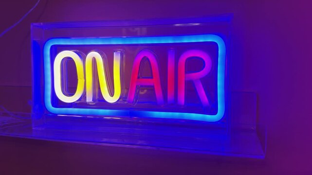 Colorful neon light featuring the text 'On Air' indicating online in tv, radio or podcast studio against a purple background
