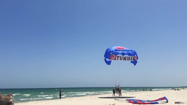 Parasailing couple adventurer landing on beautiful beach in Sousse, Tunisia under a clear sky