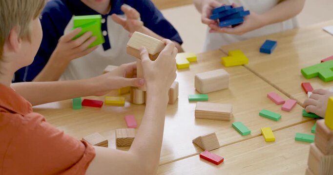 Close classroom view of children building with wooden blocks and colorful tiles on desk, practicing teamwork, creative problem solving, classwork, and back to school peer learning activity today.