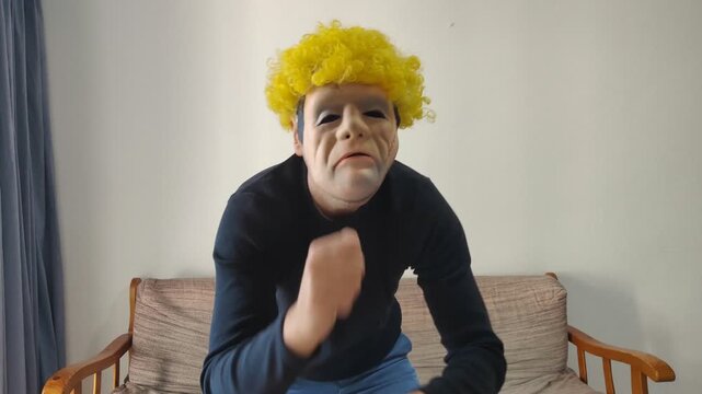 Creepy masked man with yellow wig dancing energetically