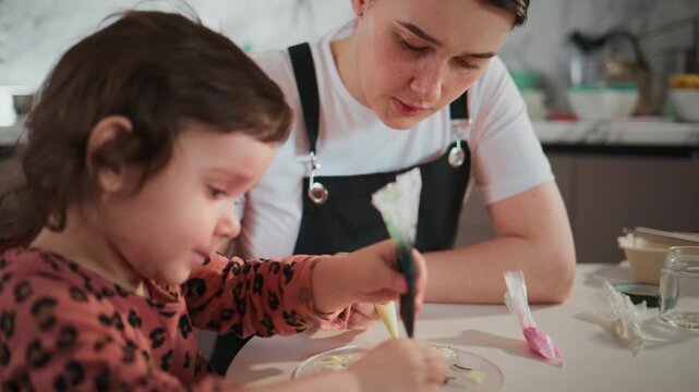 Young girl and mother crafting together in kitchen. Child focused, mother guiding gently. Creative bonding moment at home. Ideal for parenting, DIY, family, or craft content