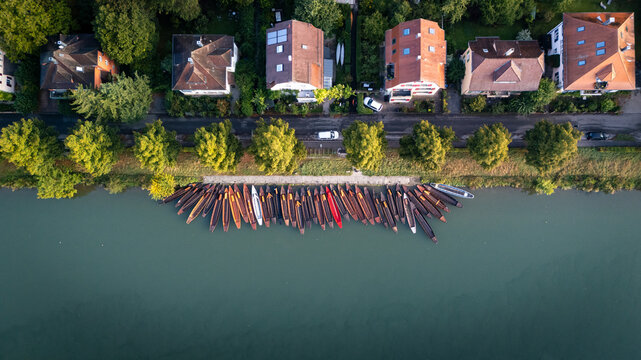 Aerial view of traditional wooden boats moored along the riverbank next to historic houses and lush green trees, Tubingen, Baden-Wurttemberg, Germany.
