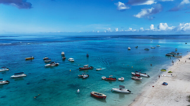 Aerial view of numerous speedboats anchored in turquoise waters along the white sandy beach with people on the shore at Trou-aux-Biches, Pamplemousses District, Mauritius.